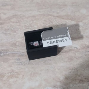 May include: A black rectangular SD card holder containing several SD cards and a Samsung SD adapter. The Samsung adapter is gray and white with the text "SD Adapter for MicroSD".