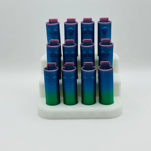 May include: A set of 15 colorful, gradient-colored, cylindrical containers with a face embossed on each. The containers are arranged in a white, three-tiered display stand.