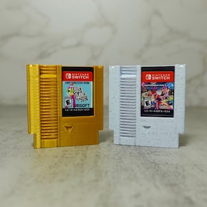 May include: Two Nintendo Switch game cartridges in custom NES-style cases. The left case is gold with "Just Dance 2021" game art. The right case is white with "Mario Kart 8 Deluxe" game art.