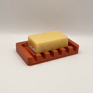 May include: A terracotta soap dish with a bar of soap on top. The dish has a ridged design to help drain water.