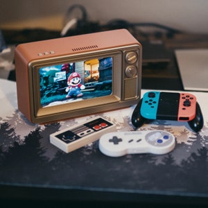May include: A retro-style television set with a brown wooden cabinet and a screen showing a video game character.  The television is on a table with a gray and black controller, a white controller, and a small gray and black controller with red buttons.