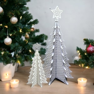May include: Two white and silver decorative Christmas trees with star toppers. The trees are made of a lattice design and are standing on a wooden surface.