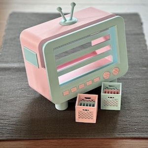 May include: A pastel pink and blue television-shaped shelf with three shelves and two small pink and blue crates.