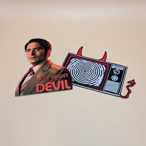 May include: Two stickers featuring a man in a suit with the text "Late Night with the Devil" and a vintage television with a spiral pattern on the screen.