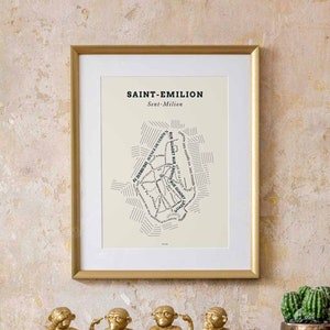 May include: Four gold monkey figurines, each with a different gesture, representing the proverb "See no evil, hear no evil, speak no evil, and do no evil". The monkeys are sitting on a wooden base in front of a framed map of Saint-Emilion, France.