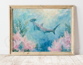 May include: A framed painting of a hammerhead shark swimming through blue water surrounded by pink coral and green seaweed. The artwork features soft, blended brushstrokes in shades of light blue, teal, and pastel pink, encased in a light wood frame.