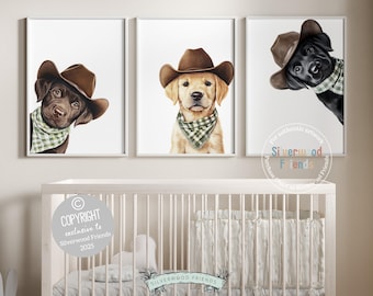 May include: Three framed prints featuring watercolor portraits of dogs wearing cowboy hats and bandanas. The dogs are a chocolate lab, a golden retriever, and a black lab. The prints are displayed above a white crib.