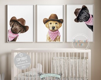 Puede incluir: Tres impresiones enmarcadas con adorables cachorros con sombreros de vaquero y pañuelos rosas. Los perros son un labrador chocolate, un golden retriever y un labrador negro. La obra de arte se exhibe sobre una cuna blanca.
