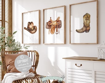 May include: Three watercolor illustrations in frames on a white wall. The illustrations are of a cowboy hat, a saddle, and a cowboy boot. The frames are all wooden and have a natural finish.