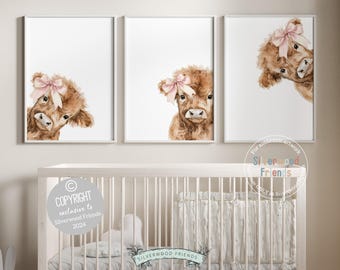 May include: Three framed wall art prints featuring watercolor illustrations of fluffy brown Highland cows. Each cow is adorned with a soft pink bow on its head. The prints are displayed in a row above a white crib, showcasing a consistent artistic style.