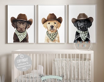 May include: Three framed art prints featuring adorable Labrador puppies wearing cowboy hats and bandanas. The puppies are a chocolate, golden, and black color. The prints are displayed above a white crib, perfect for a nursery or children's room.