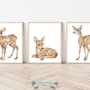 K&ouml;nnte beinhalten: Drei Aquarelle von Rehen in hellbrauner Farbe mit wei&szlig;en Flecken. Die Rehe sind in verschiedenen Posen, eines steht, eines liegt und eines steht mit dem Kopf zur Seite gedreht. Die Bilder sind in hellen Holzrahmen gerahmt und vor einem wei&szlig;en Hintergrund platziert.