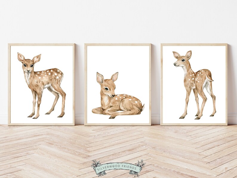 K&ouml;nnte beinhalten: Drei Aquarelle von Rehen in hellbrauner Farbe mit wei&szlig;en Flecken. Die Rehe sind in verschiedenen Posen, eines steht, eines liegt und eines steht mit dem Kopf zur Seite gedreht. Die Bilder sind in hellen Holzrahmen gerahmt und vor einem wei&szlig;en Hintergrund platziert.