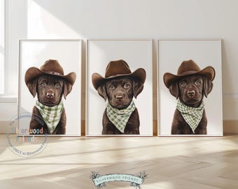 May include: Three framed prints featuring a brown Labrador puppy wearing a brown cowboy hat and a green and white checkered bandana. The artwork has a white background and is displayed on a light wood floor.