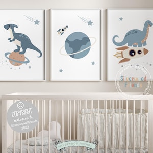 May include: Three printable wall art prints featuring a blue dinosaur on a rocket, a blue dinosaur on a planet, and a rocket ship in space. The prints have a white background with blue, orange, and yellow accents.