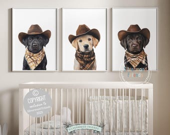 May include: Three framed prints featuring watercolor portraits of dogs wearing cowboy hats and plaid bandanas. The dogs are a black Labrador, a golden Labrador, and a chocolate Labrador. The artwork is displayed above a white crib.