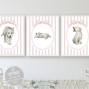 May include: Set of three pink and white striped prints with watercolor illustrations of wolf pups. Each print features a different pose of the wolf pup, including standing, lying down, and howling. The prints are framed in white.