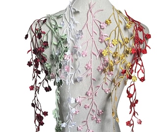 Peut inclure: Des lianes florales brodées en bordeaux, vert, blanc, rose, jaune et rouge descendent en cascade sur un mannequin. Chaque liane présente des fleurs et des feuilles délicates, créant un élément textile décoratif. Les lianes sont disposées pour mettre en valeur la variété des couleurs et des motifs.