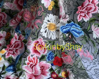 May include: Embroidered floral fabric featuring a variety of colorful flowers, including pink peonies, white daisies, and blue blossoms. The fabric has a sheer, gray background with the text "spifunbyshay".