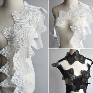 May include: White and black wavy lace trim with a geometric pattern. The lace is shown on a dress form.