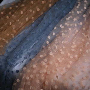 May include: Two layers of sheer fabric with polka dots. The top layer is a light brown colour and the bottom layer is a light blue colour.