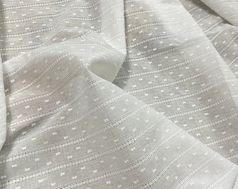 May include: Close-up of white fabric with a textured, striped pattern. The fabric has horizontal lines with small, evenly spaced dots, creating a subtle, dotted texture. The fabric is folded, showing depth and dimension.