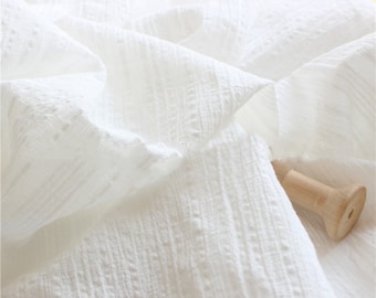 May include: White cotton fabric with a textured, woven pattern. The fabric is soft and has a slightly wrinkled appearance.