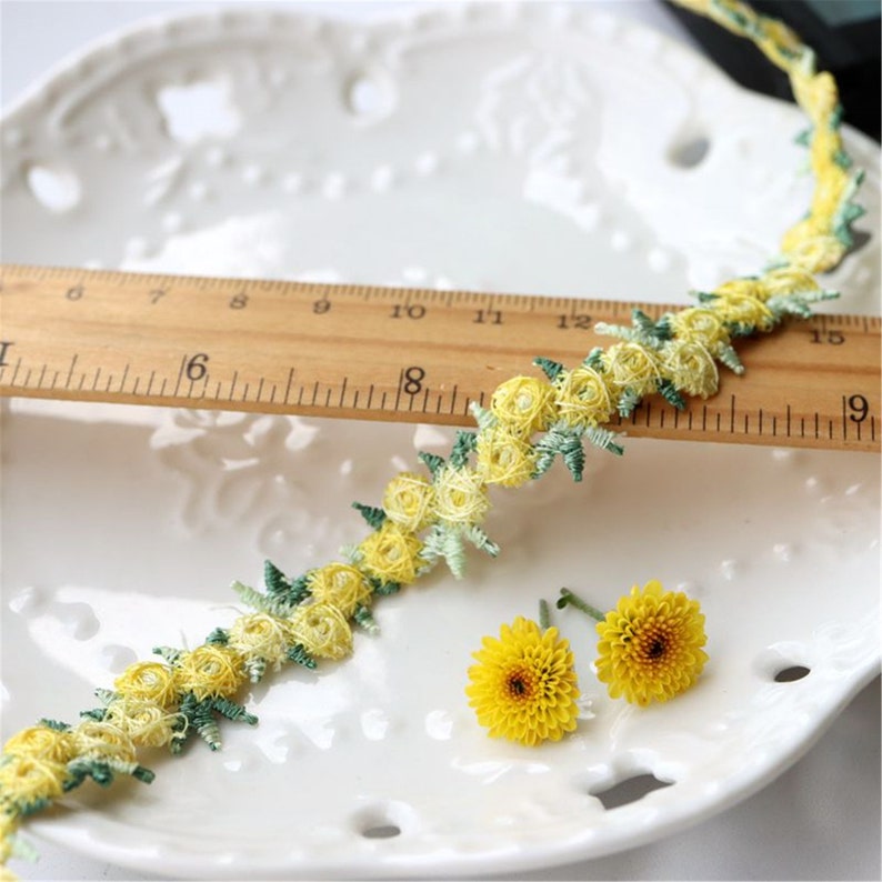 May include: Yellow and green floral trim with a ruler for scale. The trim is made of delicate fabric with small flowers and leaves.
