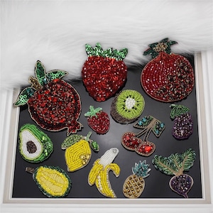 May include: Assortment of colourful fruit-shaped beaded patches, including a strawberry, pomegranate, kiwi, cherry, avocado, lemon, banana, pineapple, and a beetroot. The patches are made with sequins and beads.