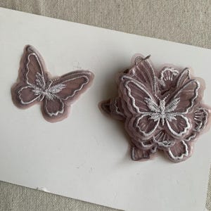 May include: Two embroidered butterfly appliques. One is a single butterfly, the other a cluster. They are a muted mauve colour with silver thread detailing. Ideal for craft projects.