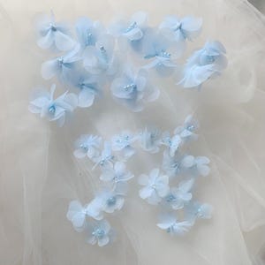 Può includere: Fiori in tessuto azzurro con centri perlati. I delicati petali a strati creano un aspetto morbido e arioso. Questi abbellimenti floreali sono ideali per l'artigianato, il cucito o per aggiungere un tocco di eleganza.