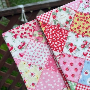 Könnte beinhalten: Ein Stoff mit einem Patchwork-Design aus verschiedenen Quadraten mit Erdbeermustern, Blumenmotiven und Punkten in Rot-, Rosa-, Gelb- und Blautönen. Der Text "Sweet strawberry" und "Berry" ist auf einigen der Stoffquadrate aufgedruckt.