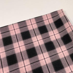 May include: A skirt featuring a classic plaid pattern in shades of light pink, black, and grey. The fabric displays a repeating grid design with intersecting horizontal and vertical lines, creating a structured and uniform checkered appearance throughout.