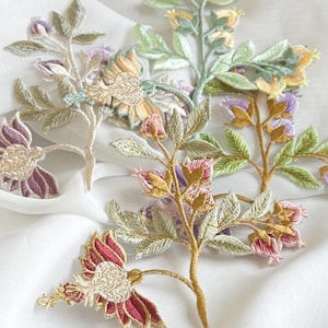 Könnte beinhalten: Gestickte Blumenapplikationen in verschiedenen Farben, darunter Rot, Lila, Gelb und Grün. Die Applikationen weisen detaillierte Nähte auf weißem Hintergrund auf. Die floralen Designs umfassen Blätter und Blüten.