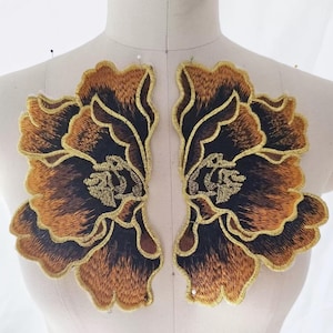 Op de afbeelding: Twee geborduurde bloemenapplicaties. Elke applicatie heeft een groot bloemmotief met bruin, zwart en goudkleurig garen. De bloemen zijn gedetailleerd met ingewikkelde steken en omrand met goudkleurig garen. De applicaties worden op een mannequin getoond.