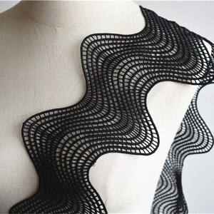 May include: Black wavy lace trim with a geometric pattern. The lace is delicate and intricate, with a scalloped edge.