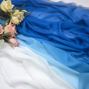 May include: A blue ombre fabric with a white border. The fabric is draped over a white surface with a bouquet of pink and white roses.
