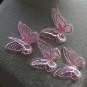 May include: A collection of pink butterfly appliques with sheer wings and detailed embroidery. The butterflies are in different positions, highlighting their intricate design and soft colour palette. These appliques are suitable for craft projects.