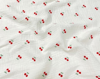 May include: White fabric with a repeating pattern of red cherries. The fabric has a slightly textured surface.