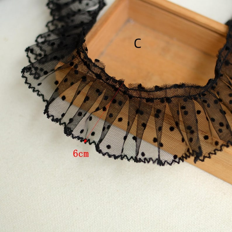 May include: Black lace trim with white polka dots. The trim is 6 cm wide and has a ruffled edge.