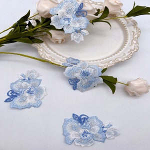 Pode incluir: Quatro apliques de flores bordadas em azul e branco. Os apliques são delicados e intrincados, com um design floral. São perfeitos para adicionar um toque de elegância a qualquer projeto.