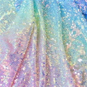 May include: A close-up of iridescent rainbow fabric with sequins. The fabric is folded and the sequins are catching the light.
