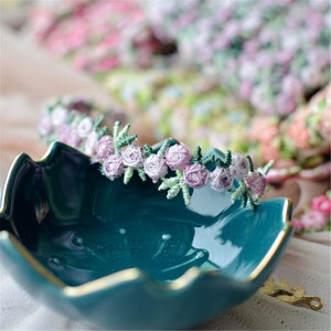 May include: A teal blue ceramic dish with a gold rim, featuring a delicate floral trim of pink and white flowers with green leaves.
