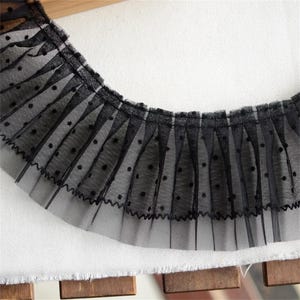 May include: Black lace trim with a dotted pattern. The lace is gathered and has a ruffled edge.