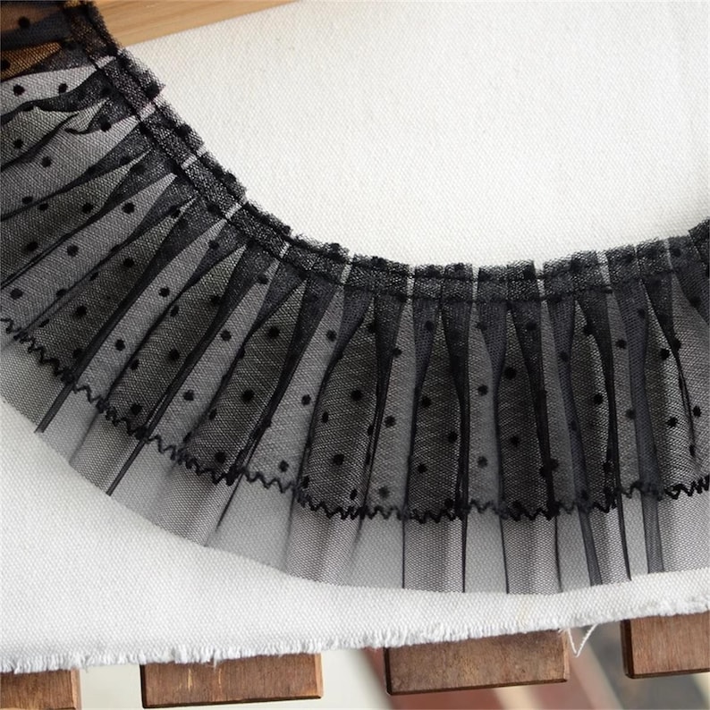 May include: Black lace trim with a dotted pattern. The lace is gathered and has a ruffled edge.
