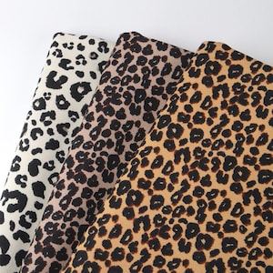 May include: Three fabric swatches featuring a leopard print design. The swatches are in various shades of brown, beige, and white.