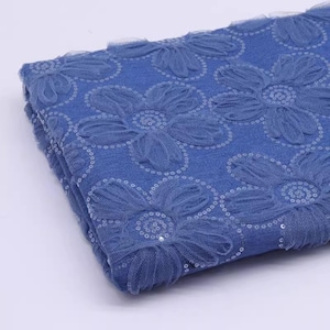 May include: Blue fabric with a floral pattern and sequins. The fabric is folded in half and the sequins are visible on the surface.