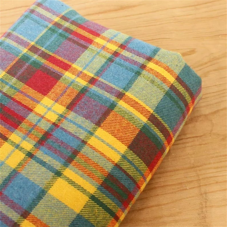 K&ouml;nnte beinhalten: Ein gefalteter Stoff mit einem farbenfrohen Karomuster. Das Design zeigt sich kreuzende Linien in Blau-, Gelb-, Rot-, Gr&uuml;n- und Oranget&ouml;nen. Der Stoff ist wahrscheinlich ein gewebtes Material, m&ouml;glicherweise Baumwolle oder Wolle.