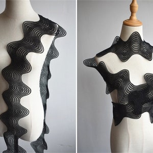 May include: Black wavy lace trim with a scalloped edge. The lace is shown on a white mannequin form.