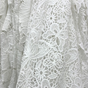 Op de afbeelding: Wit kant met een delicaat bloemenpatroon. De kant is ingewikkeld en heeft een zachte, vloeiende textuur.